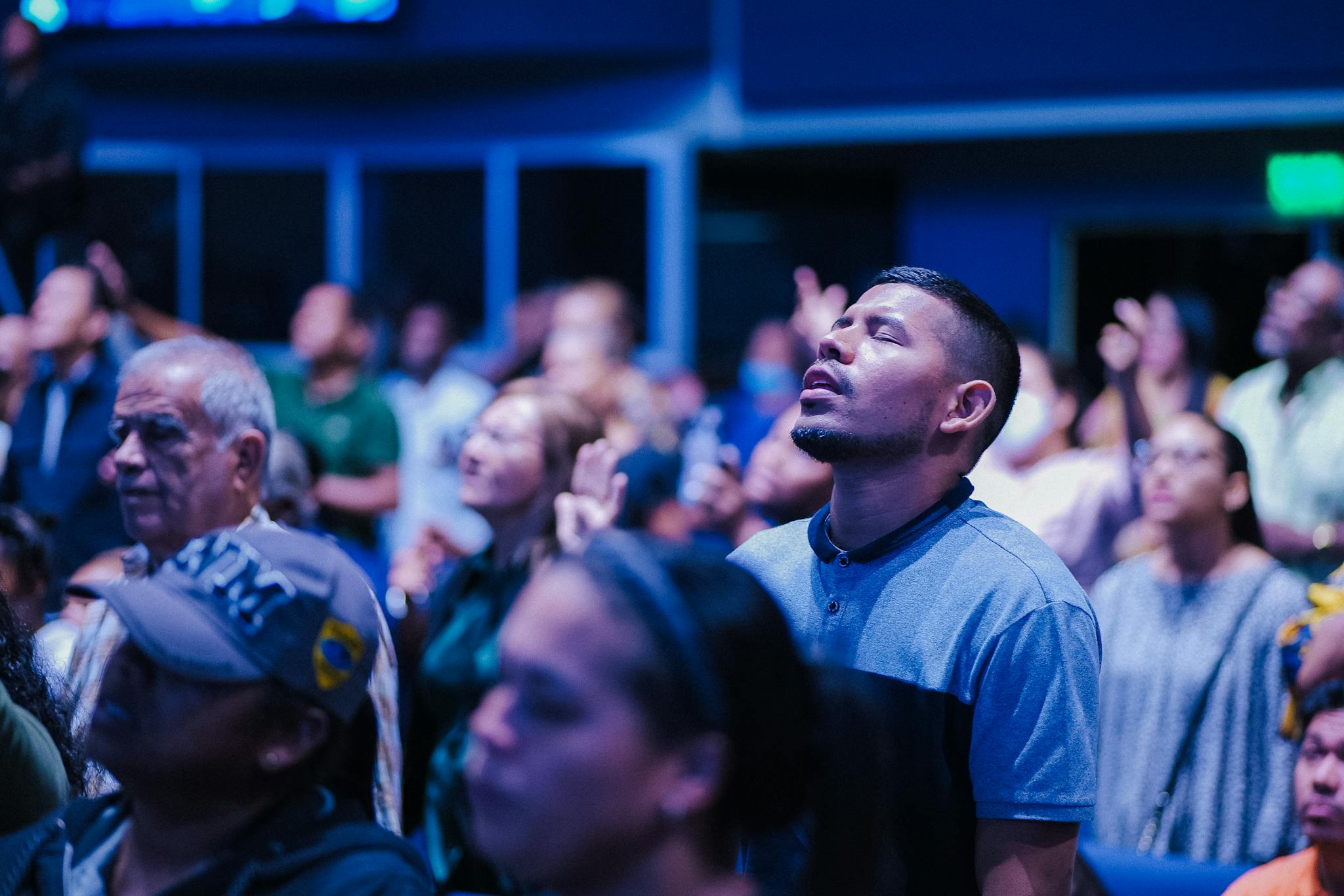 A crowd participates in a contemplative indoor prayer event, eyes closed and focused in spiritual meditation.