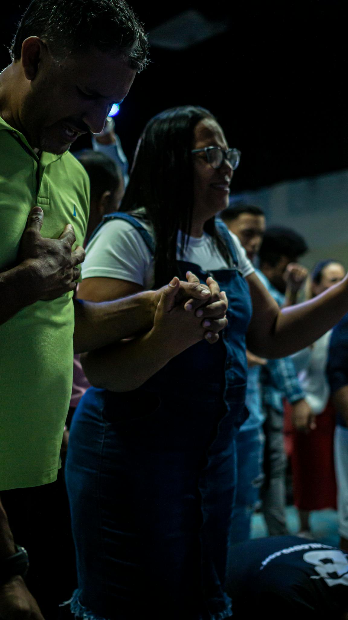 A diverse group of people holding hands in prayer during a worship gathering, eyes closed in unity.