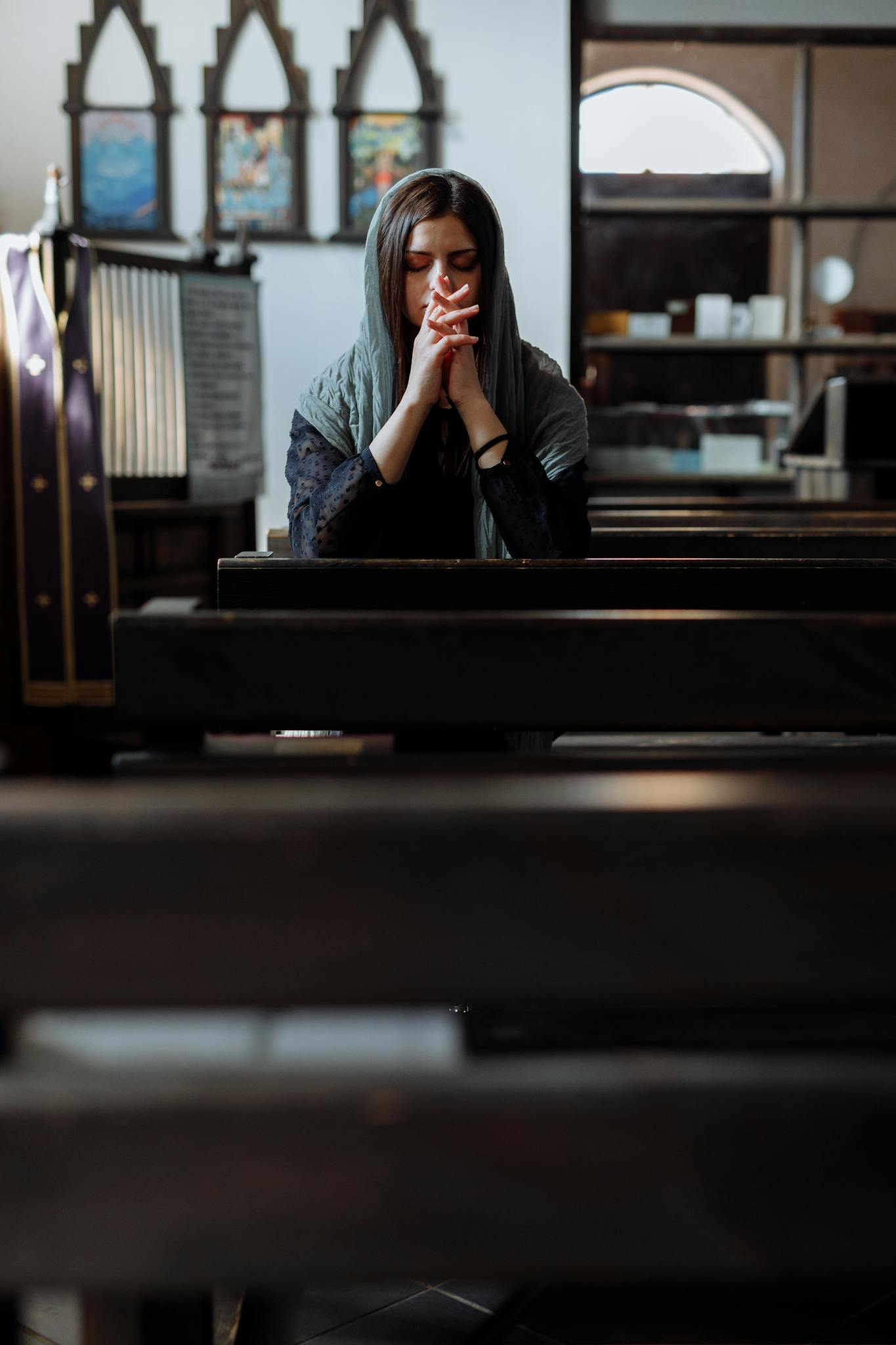 A woman meditates in a church, eyes closed and hands clasped, in peaceful reflection.