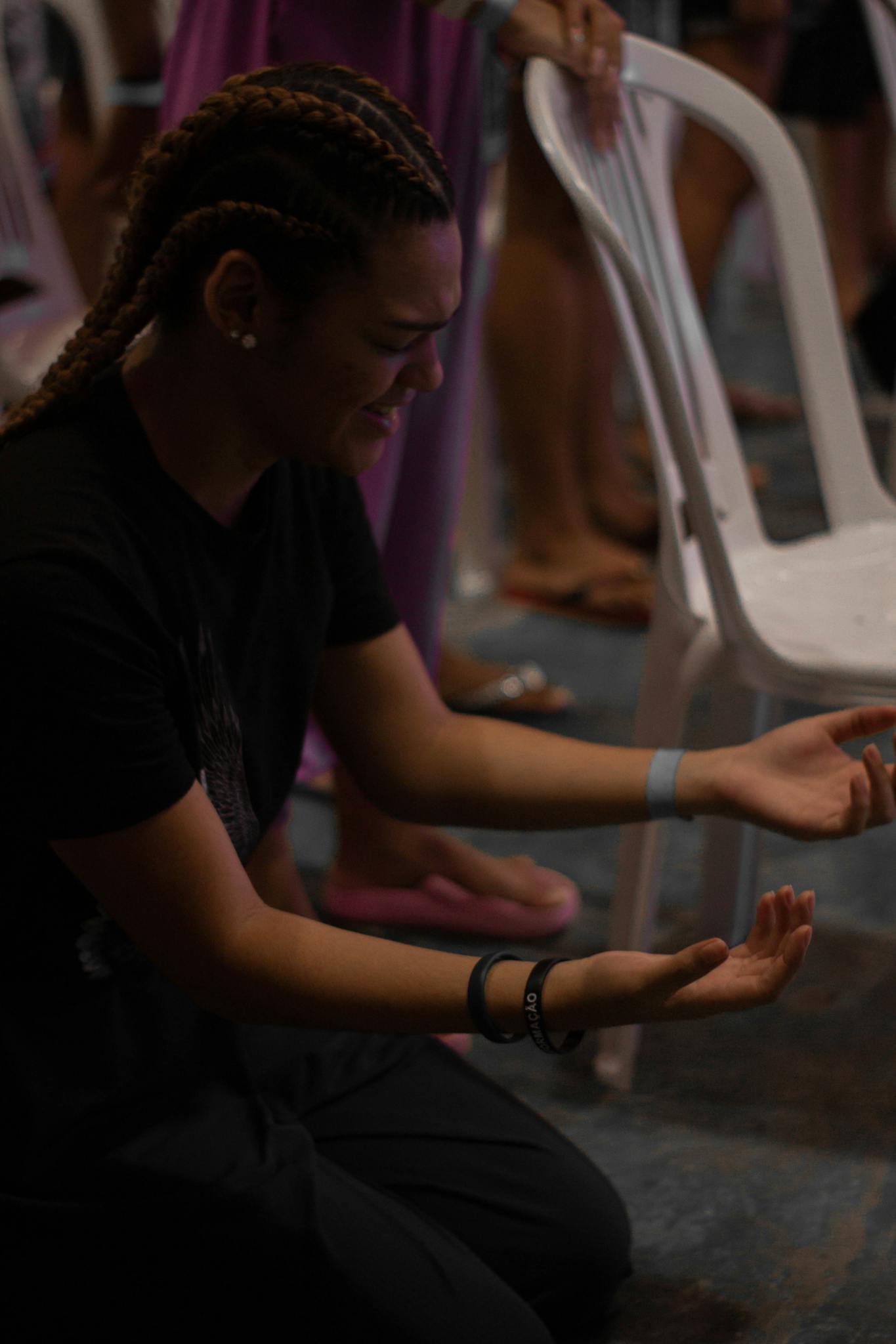 A woman with braided hair kneels in prayer, hands open, capturing a moment of spiritual devotion.